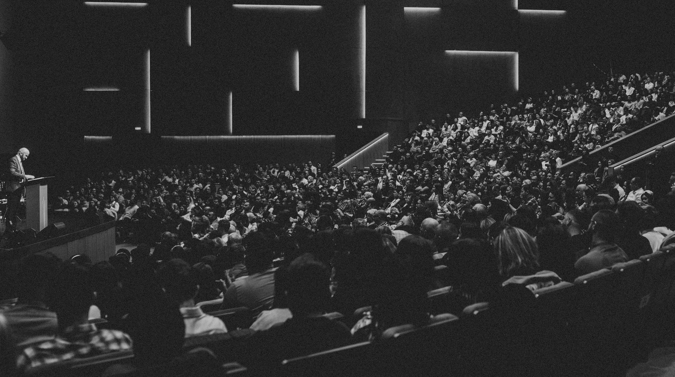 A speaker addressing a seated audience from the lectern of a conference theatre